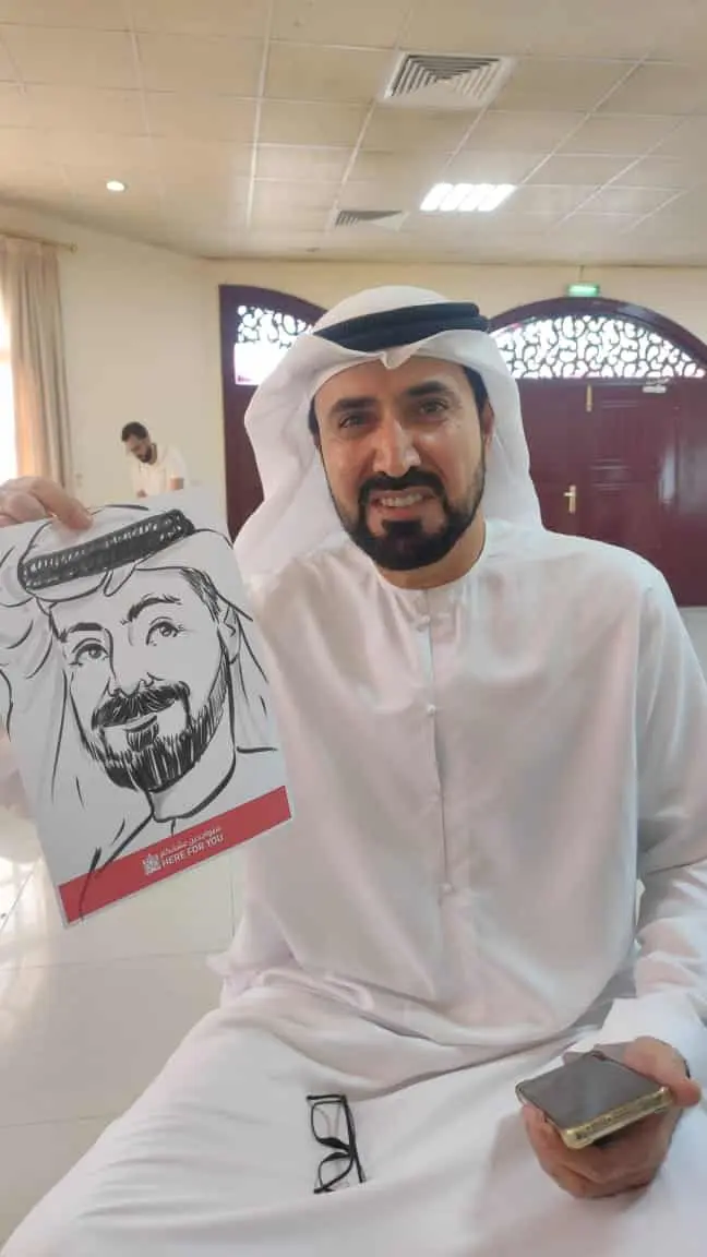 Emirati guest in a white kandura smiling beside his live caricature at a staff event
