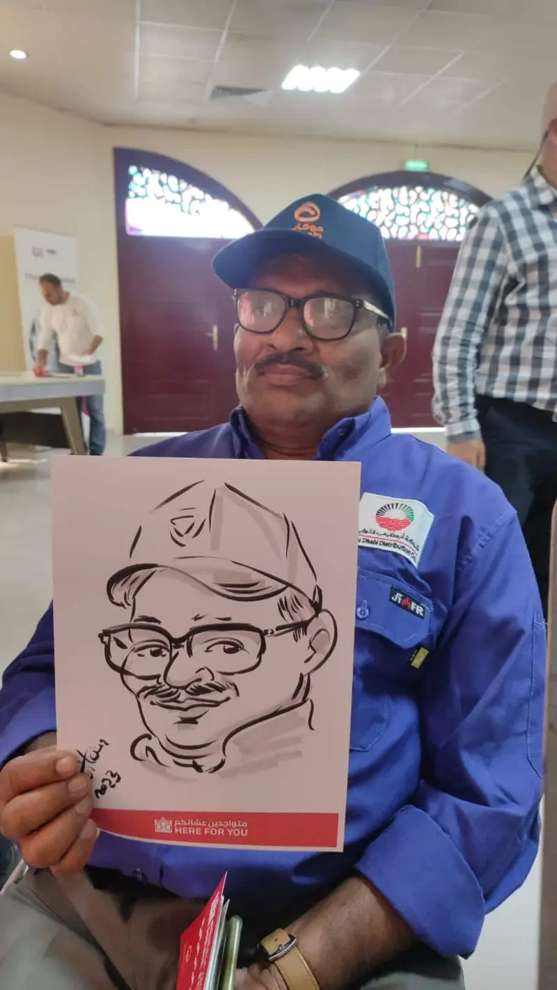 Guest in a cap and glasses holding his live caricature, drawn in black marker at a company event